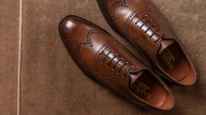 Pair of brown leather wingtip Oxford dress shoes with brogue detailing, displayed on a suede background.
