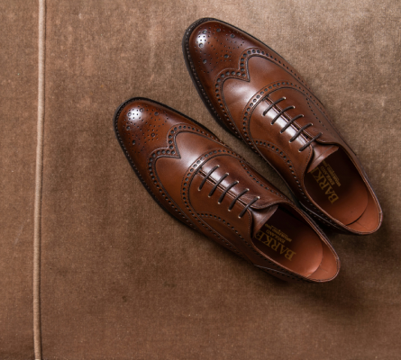 Pair of brown leather wingtip Oxford dress shoes with brogue detailing, displayed on a suede background.