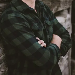 Man in a green plaid flannel shirt with arms crossed – spring layering outfit for guys