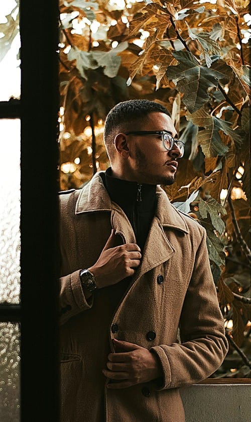 Man in camel coat and dark turtleneck looking out near autumn foliage – refined smart casual wear for men classic outfit