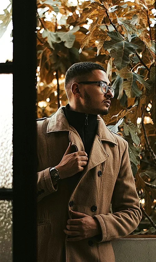 Man in camel coat and dark turtleneck looking out near autumn foliage – refined smart casual wear for men classic outfit