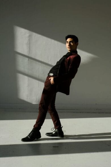Man in burgundy suit and black dress shirt leaning in dramatic sunlight – elevated smart casual outfit