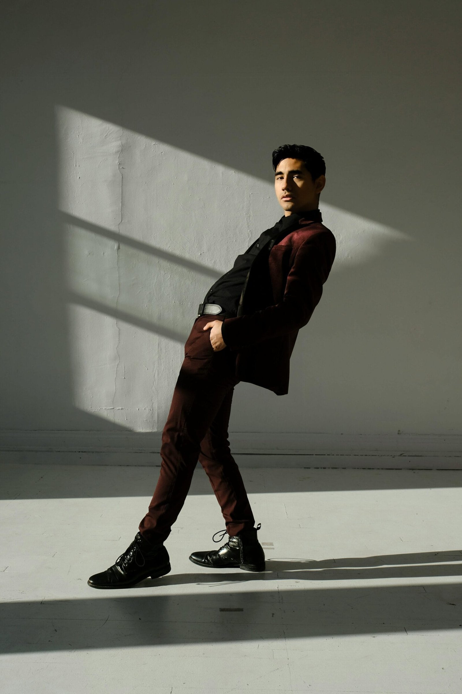 Man in burgundy suit and black dress shirt leaning in dramatic sunlight – elevated smart casual outfit