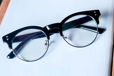 Close-up of classic browline eyeglasses with black upper frames and clear lenses on a white surface.