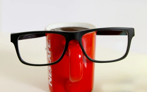 Black rectangular eyeglasses resting on the rim of a red Nescafé coffee mug.