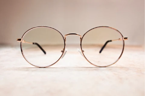 Minimalist round eyeglasses with thin gold frames, positioned on a soft, neutral surface.