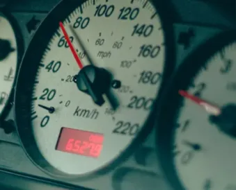 Car speedometer gauge showing needle at approximately 60 mph with digital odometer display, photographed with teal/cyan color filter