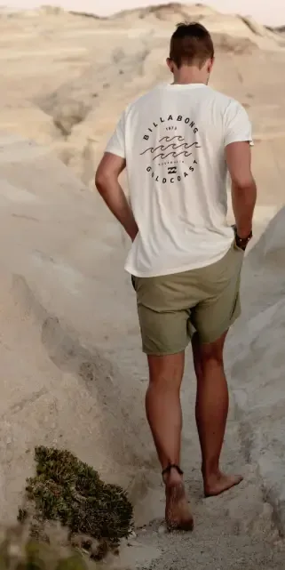 billabong Man walking barefoot on a rocky path wearing a Billabong t-shirt and khaki shorts.