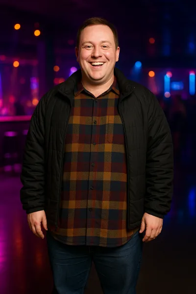 short men's style - short looks A smiling man in a black jacket and plaid shirt showcases short men's style in a dimly lit, colorful venue.