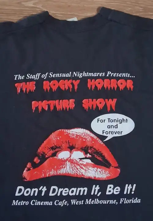 Black t-shirt featuring red lips and dripping text promoting The Rocky Horror Picture Show with the phrase “Don’t Dream It, Be It!” at Metro Cinema Cafe in West Melbourne, Florida.