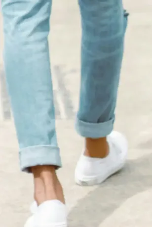 Man walking in cuffed light wash men's Spring denim jeans with white slip-on sneakers.
