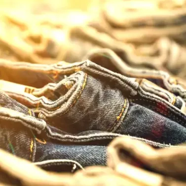 Close-up of stacked men's Spring denim jeans in various washes with detailed stitching and warm lighting.
