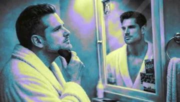 Man using a gua sha tool along his jawline in the mirror to reduce face bloating.