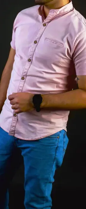 Man wearing a light pink short sleeve button-up shirt with blue pants against a dark background