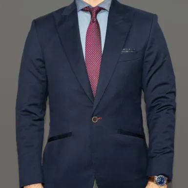 Man wearing a fitted single button navy suit jacket, light blue dress shirt, and patterned red tie, showing tailoring details that can help create a taller appearance.