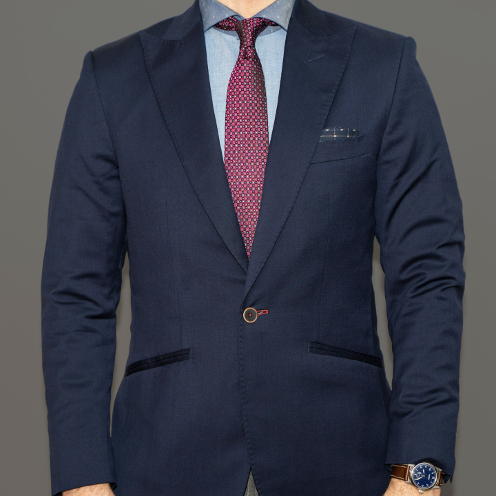 Man wearing a fitted single button navy suit jacket, light blue dress shirt, and patterned red tie, showing tailoring details that can help create a taller appearance.