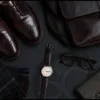 Dark Academia Accessories for men including oxblood brogues, leather messenger bag, watch, tortoiseshell glasses, and wool scarf.