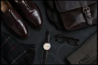 Dark Academia Accessories for men including oxblood brogues, leather messenger bag, watch, tortoiseshell glasses, and wool scarf.