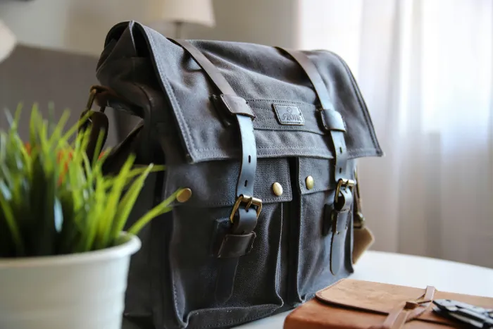 Black waxed canvas satchel with leather straps and brass hardware styled as a Dark Academia Accessory.