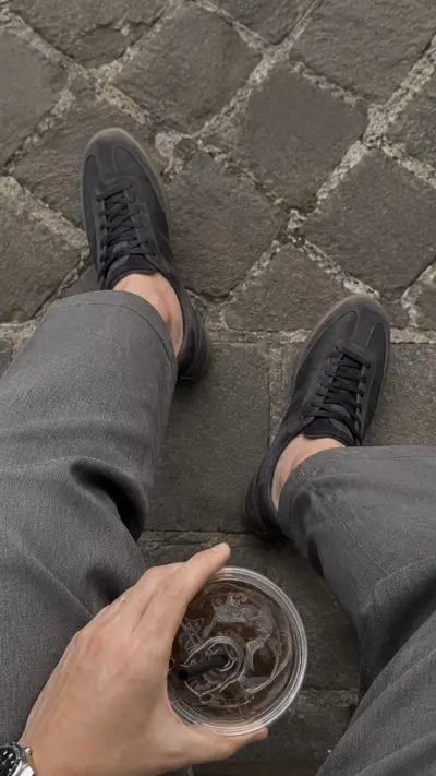 Gray trousers and dark sneakers showing how to wear monochrome with tonal footwear.