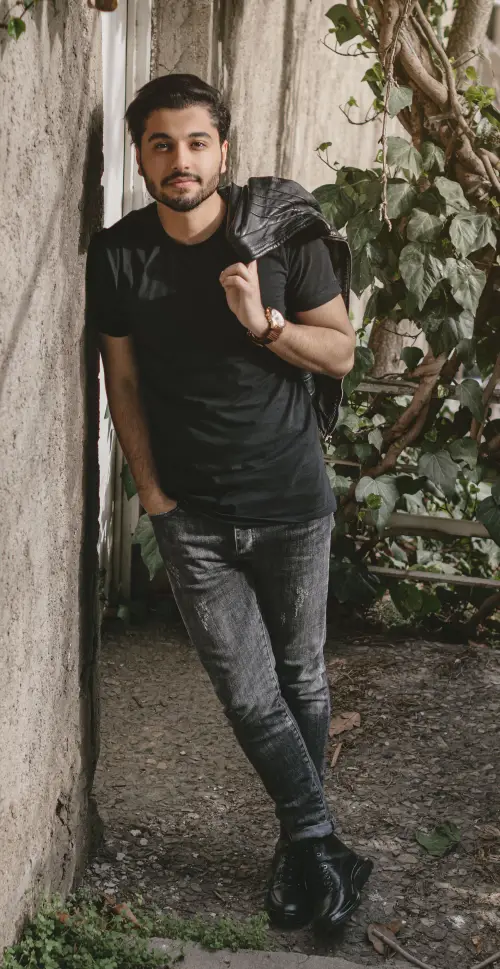 Man wearing an all black outfit with a black T-shirt, faded black jeans, black boots, and a leather jacket.