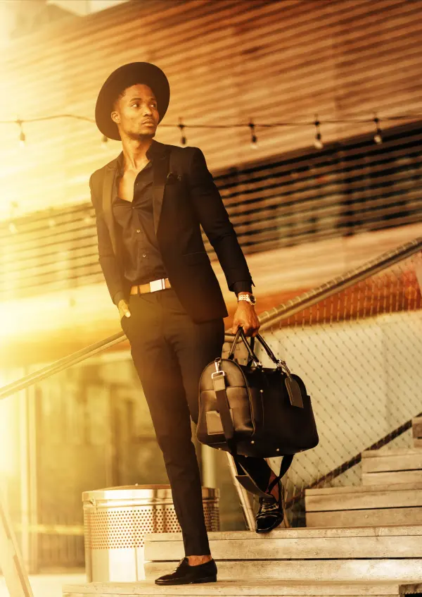 Man wearing an all black outfit with a black suit, black shirt, black loafers, and wide-brim hat.