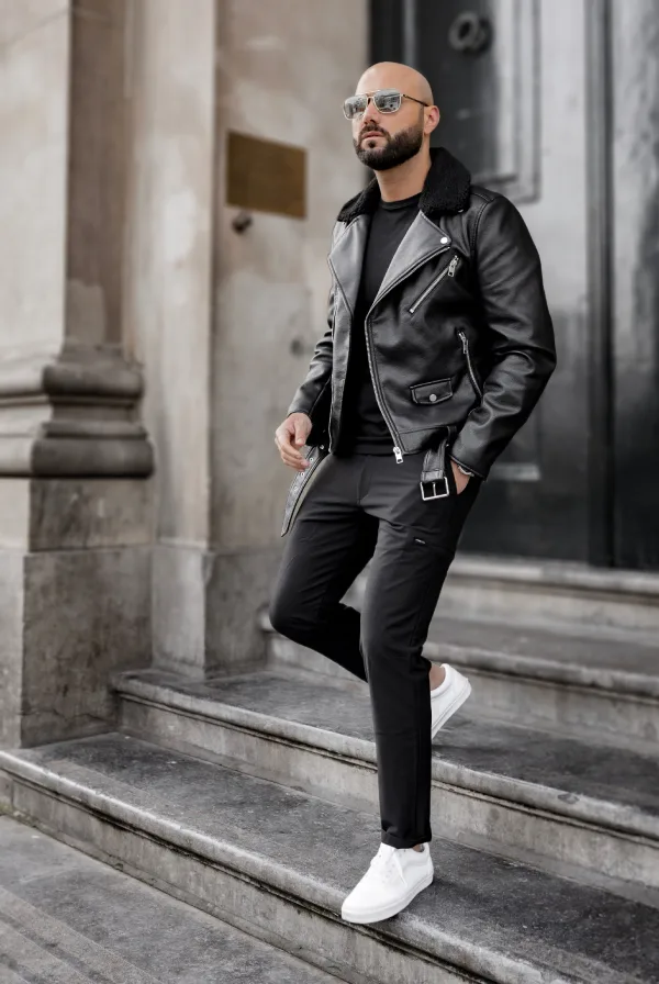 Man wearing an all black outfit with a black leather biker jacket, black T-shirt, slim black pants, and white sneakers.