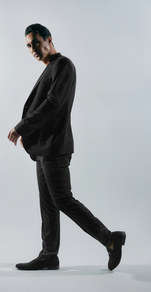 Man wearing an all black outfit with a black blazer, trousers, and dress shoes.