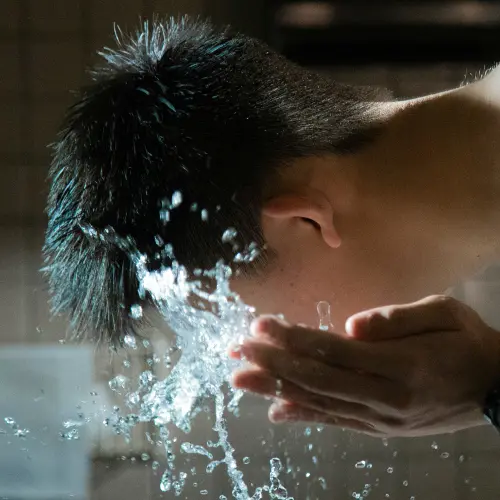 Man splashing water on his face while cleansing as part of a skincare routine for men.