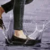Can Suede Shoes Get Wet? Person wearing brown suede shoes stepping through a puddle in heavy rain.