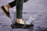 Can Suede Shoes Get Wet? Person wearing brown suede shoes stepping through a puddle in heavy rain.