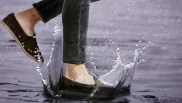 Can Suede Shoes Get Wet? Person wearing brown suede shoes stepping through a puddle in heavy rain.