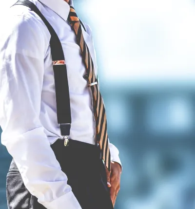 Man wearing black clip-on suspenders with dress trousers and a white shirt, illustrating do you wear a belt with suspenders.